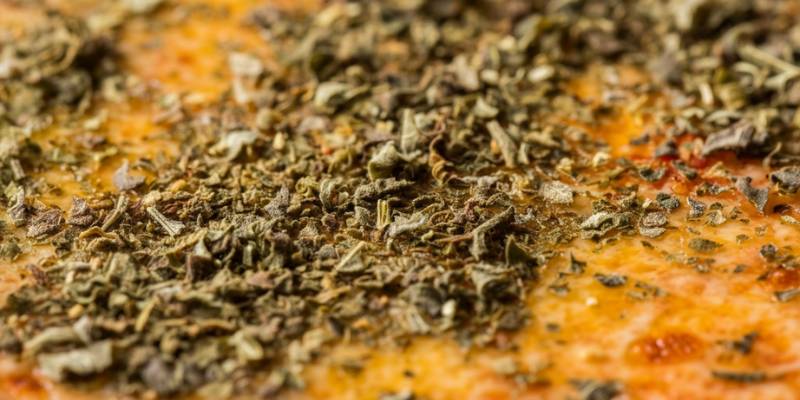 A close-up of dried basil sprinkled on a freshly baked pizza with melted cheese and tomato sauce