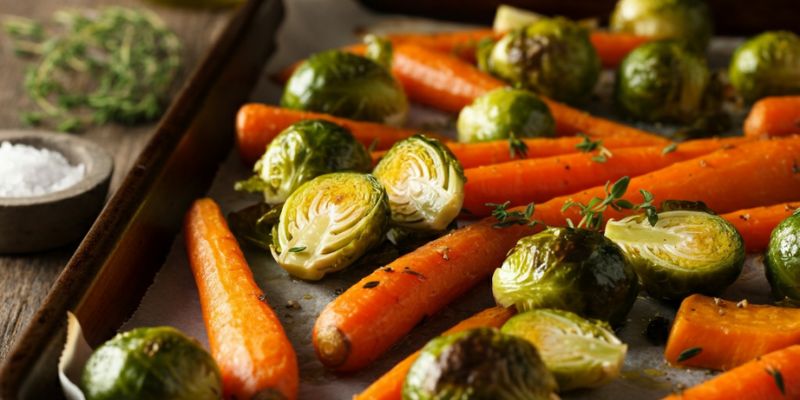 A tray of roasted carrots, Brussels sprouts, and sweet potatoes, glistening with olive oil and sprinkled with thyme, fresh out of the oven